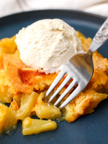 A vegan pineapple dump cake with vanilla ice cream on top and a fork picking up a piece of pineapple.