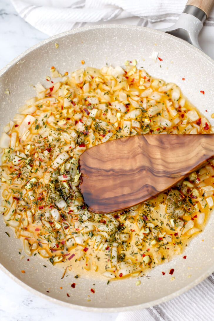 Sautéed onion, garlic, and herbs in a skillet.