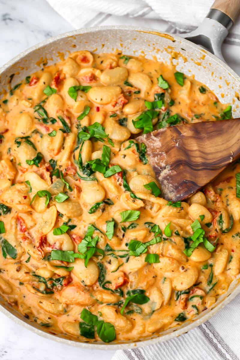 A pan full of creamy vegan Marry Me butter beans with basil on top.
