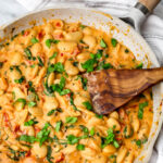 A white skillet filled with Marry Me Butter Beans with a wooden spoon stirring it.