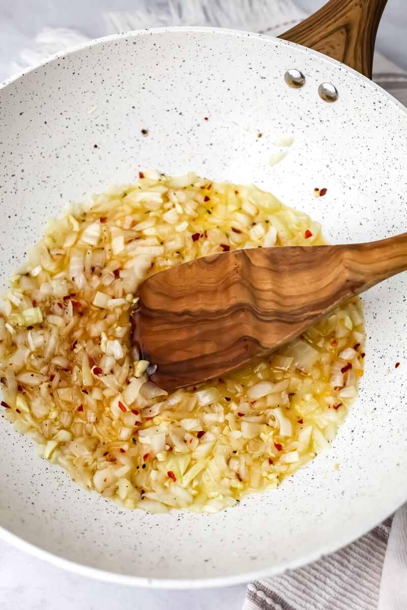 Sauteed onions and garlic with red pepper flakes in a white skillet.