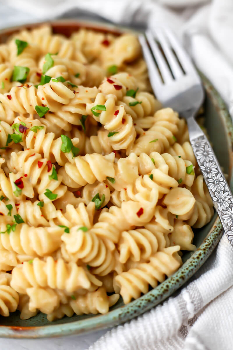 Creamy white bean pasta sauce mixed with spiral pasta with parsley and red pepper flakes on top and a fork on the side.