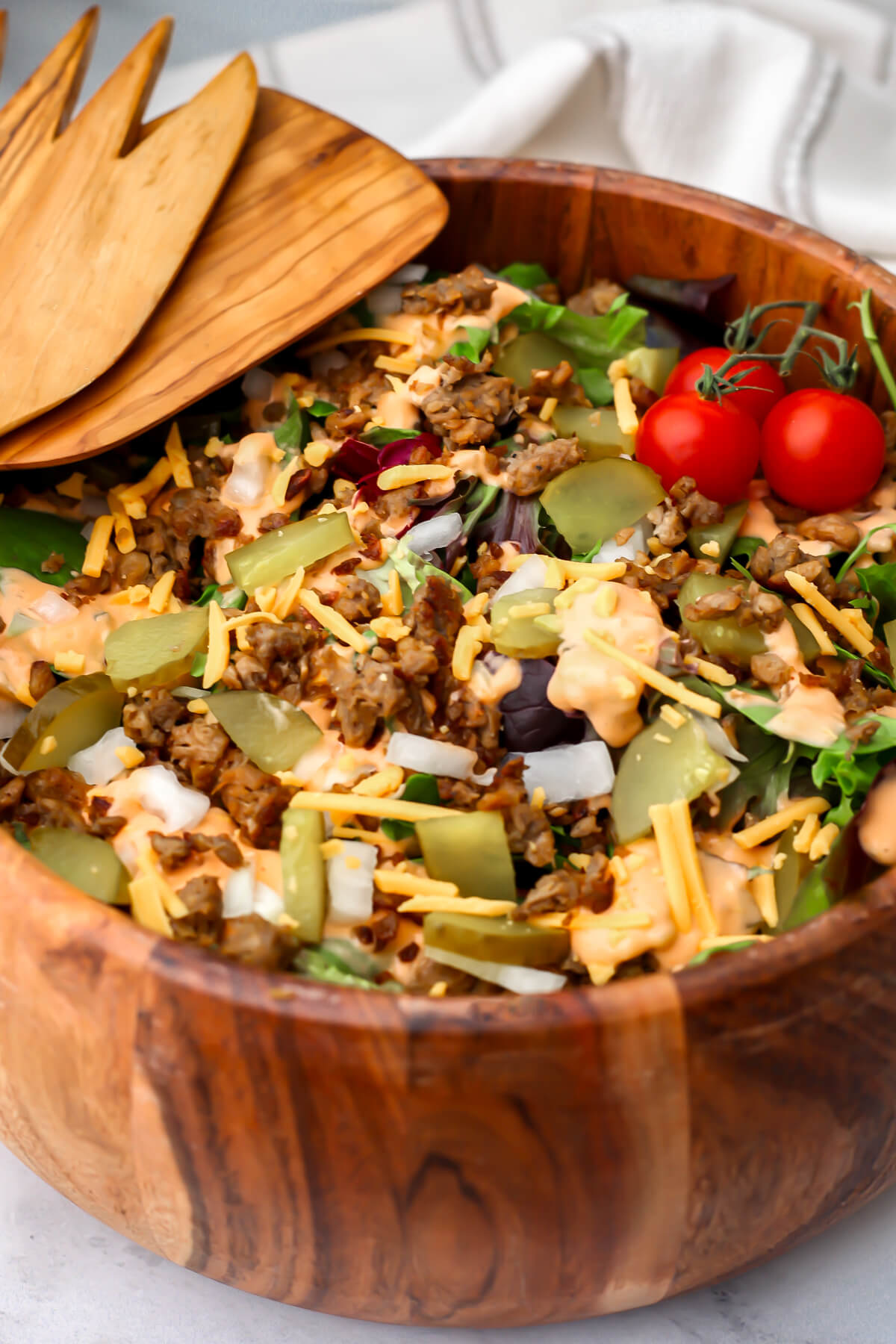 A wooden salad bowl filled with vegan Big Mac salad with onions, pickles, cheese, and vegan burger on top.