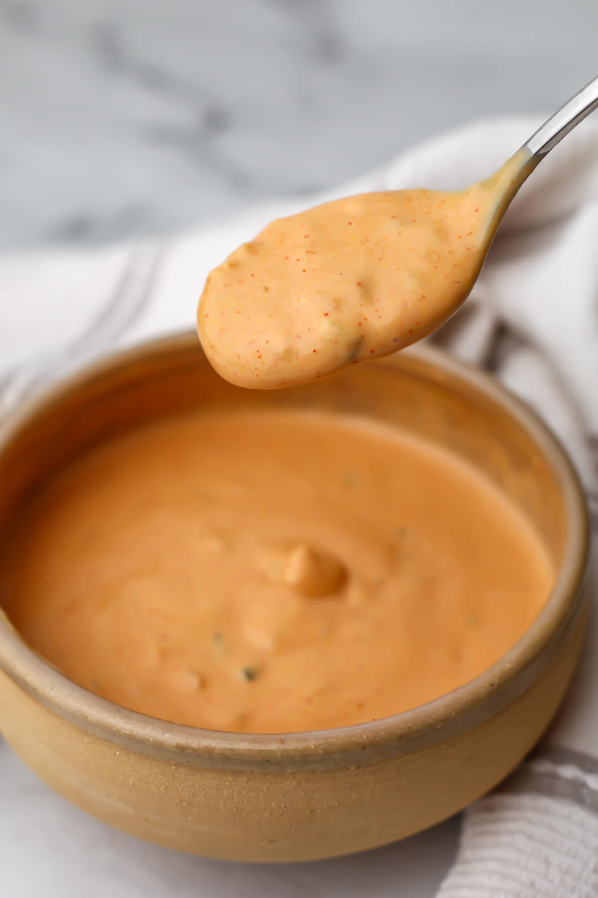 A spoonful of vegan Big Mac sauce being held over a bowl.