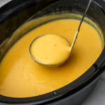 A ladle scooping out creamy vegan potato soup out of a slow cooker.