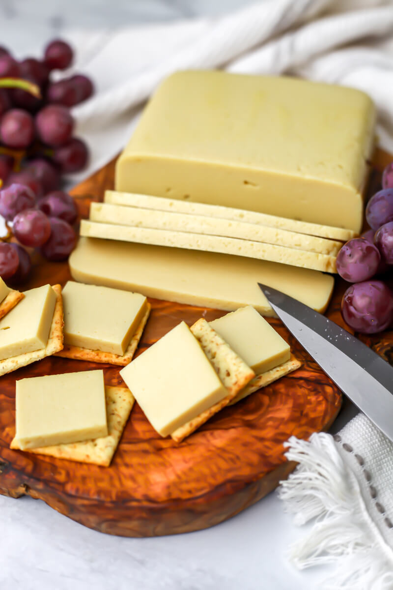 Vegan cheese made from silken tofu slice and put on crackers on a wooden cutting board.