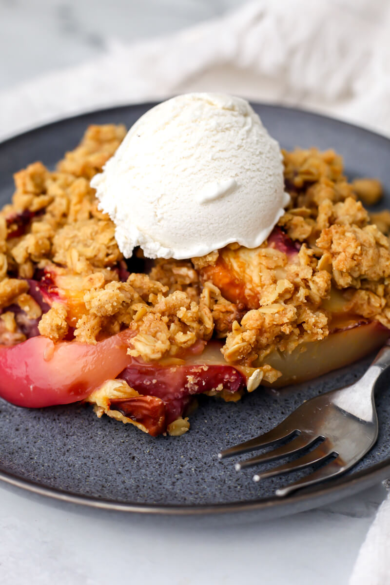 A vegan peach crisp on a blue plate with a scoop of vanilla ice cream on top.