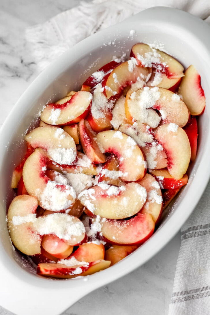 Sliced peaches sprinkled with corn starch and sugar in a baking dish.