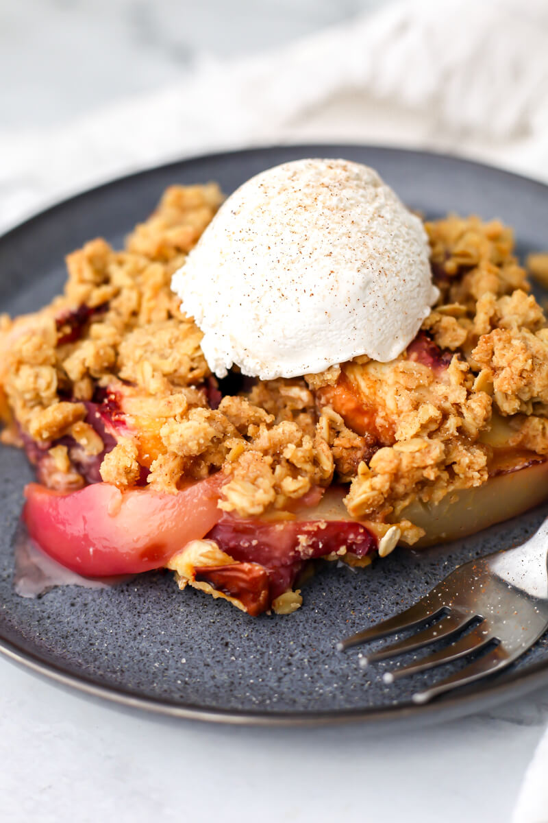 A vegan peach crisp on a blue plate with a scoop of ice cream and a sprinkle of cinnamon on top.
