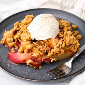 A vegan peach crisp with a scoop of vanilla ice cream on top and a fork on the side.