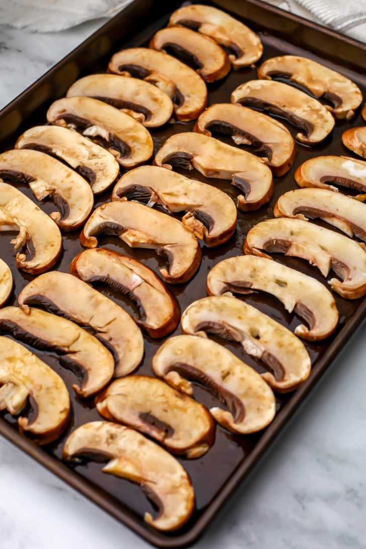 Slices of portobello mushrooms marinating on a baking sheet.