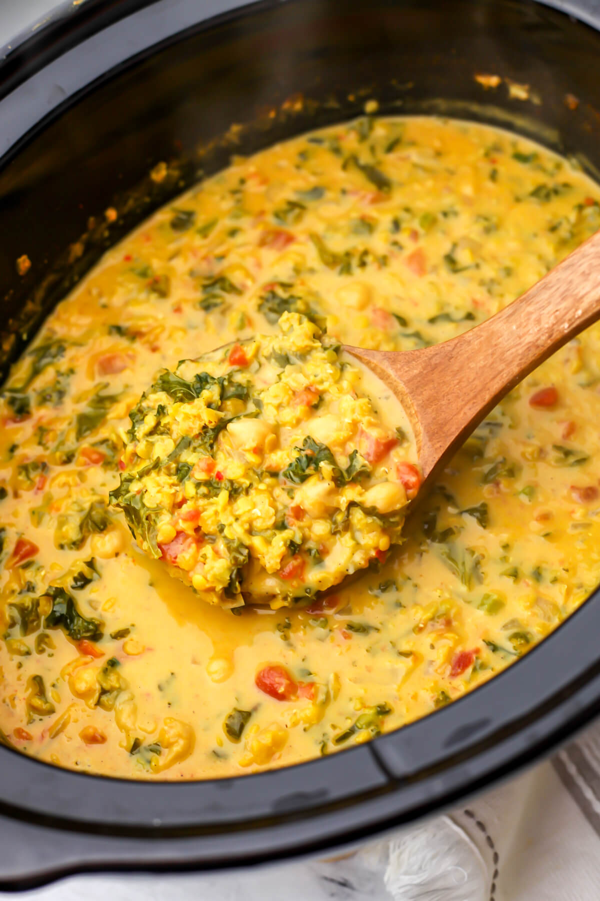 Red lentil dahl with chickpeas and kale in a creamy coconut sauce being scooped out of a slow cooker with a wooden ladle.
