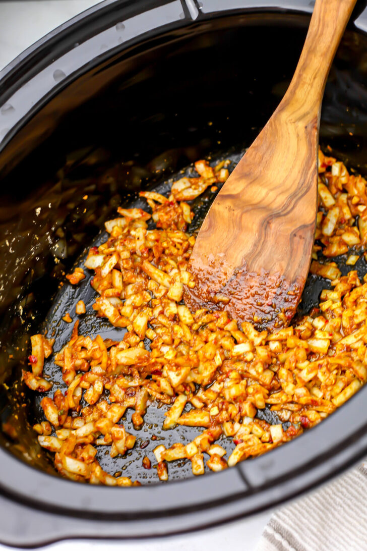 Onions, garlic, ginger, and spices in oil at the bottom of a slow cooker.