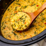 Vegan red lentil dahl with chickpeas and kale being scooped out of a slow cooker with a wooden ladle.