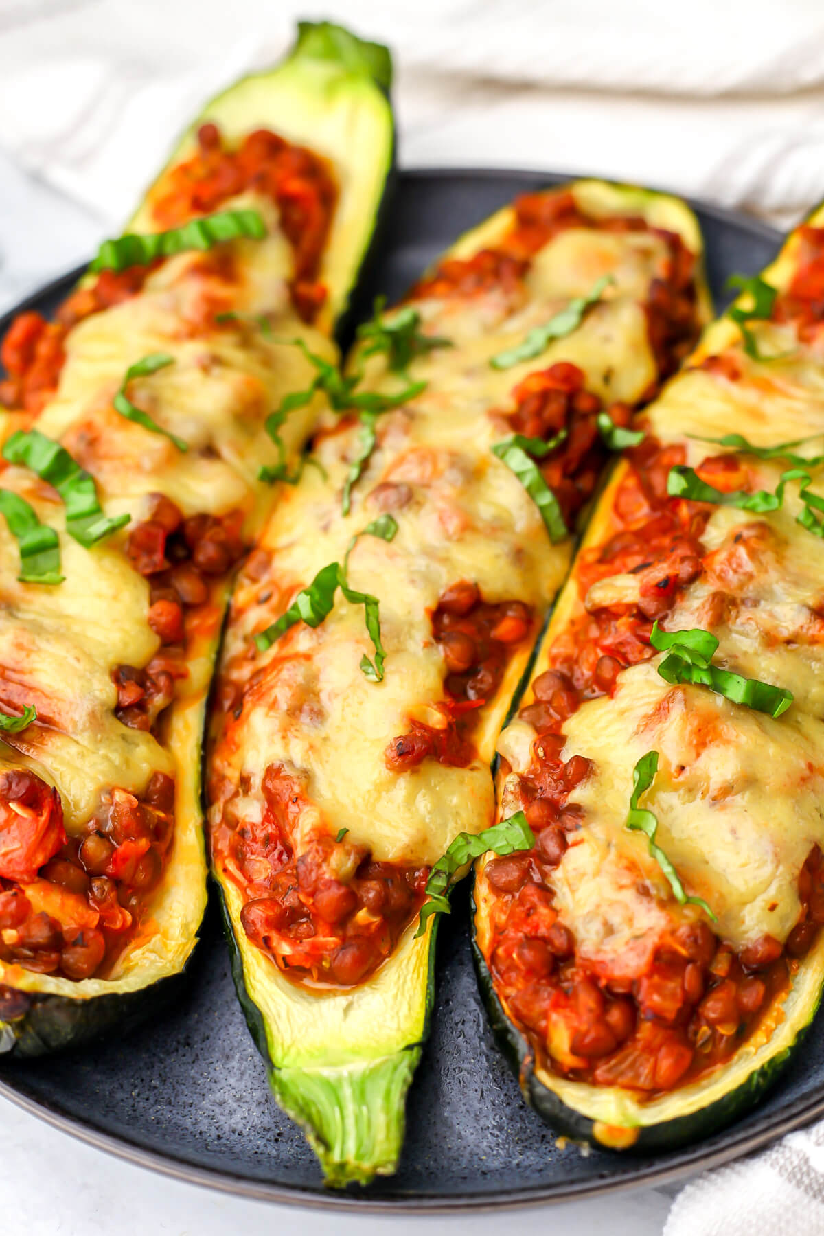 Three lentil stuffed zucchini boats on a blue plate topped with cheese.