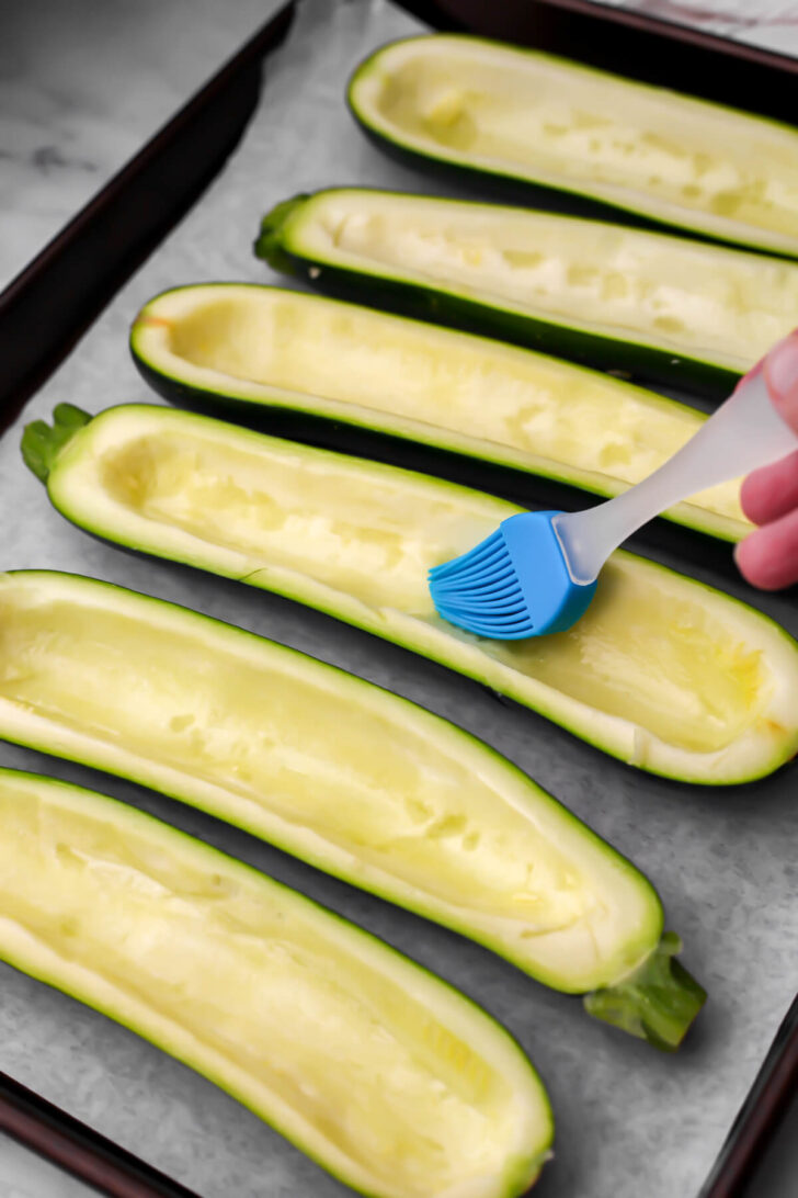 Zucchini with the middle scraped out being brushed with olive oil.