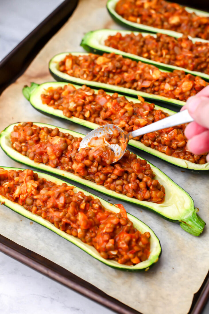 Filling the zucchini boats with the lentil pizza mixture.