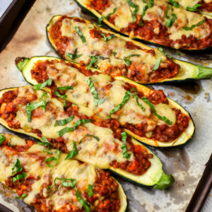 Lentil stuffed vegan zucchini boats topped with vegan cheese and basil on a baking sheet.