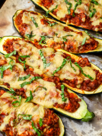 Lentil stuffed vegan zucchini boats topped with vegan cheese and basil on a baking sheet.