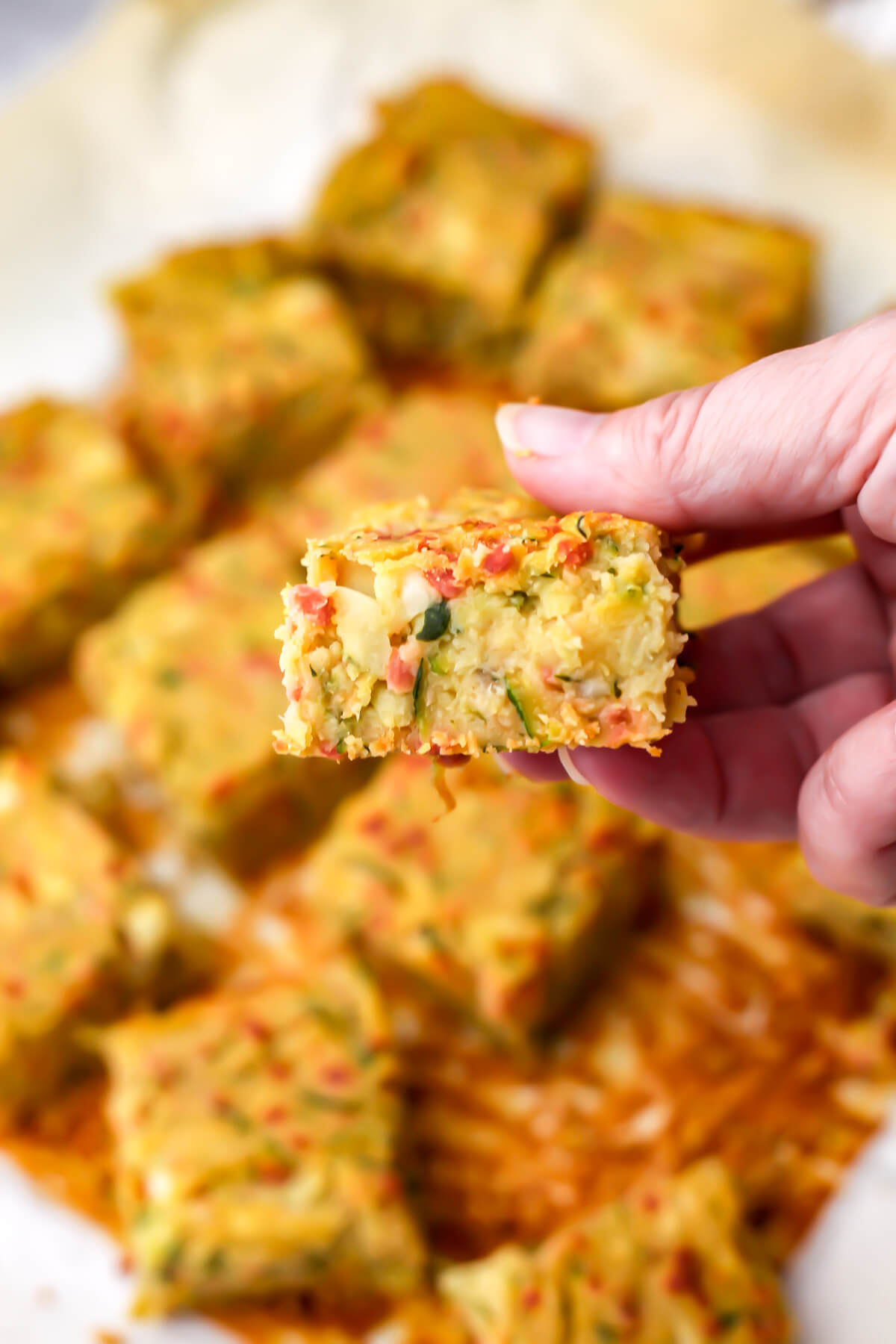 A square of a vegan zucchini slice being held up in someone's hand.