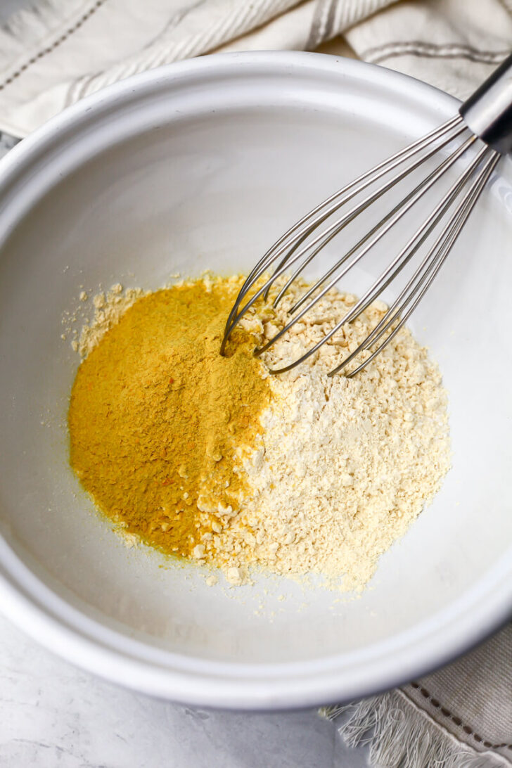 Chickpea flour, nutritional yeast, and salt in a white bowl to make vegan zucchini slice.