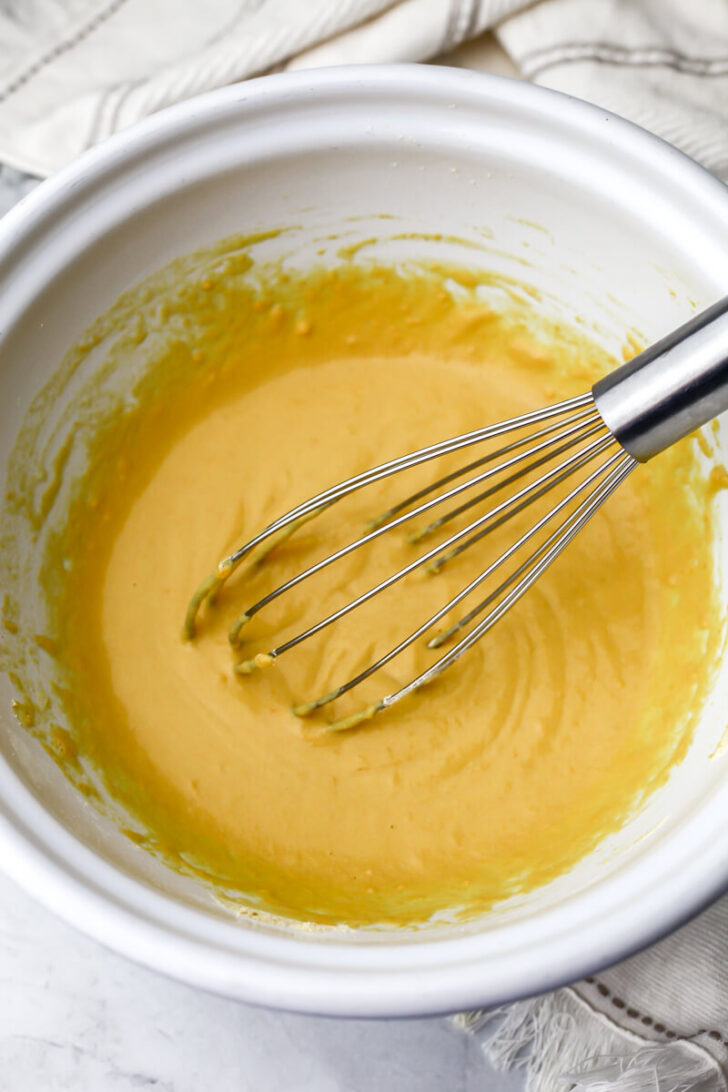 Chickpea flour, nutritional yeast, and salt with water and olive oil added in a white bowl to make vegan zucchini slice.