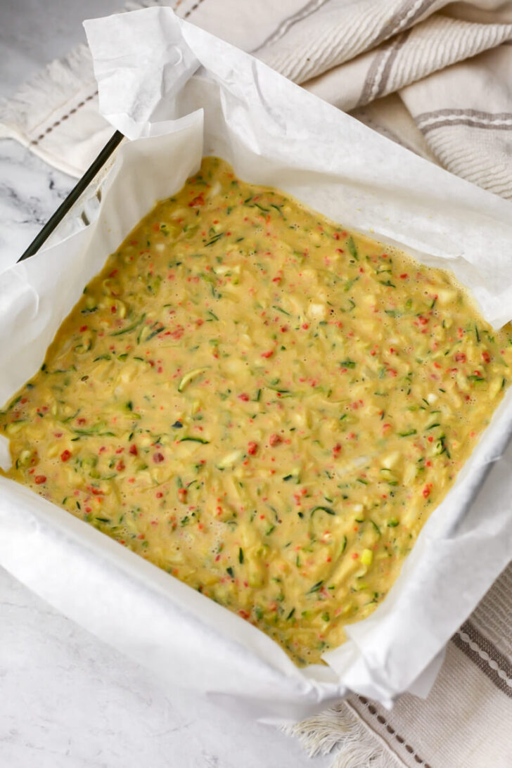 Vegan zucchini slice batter added to a baking dish lined with parchment paper. 