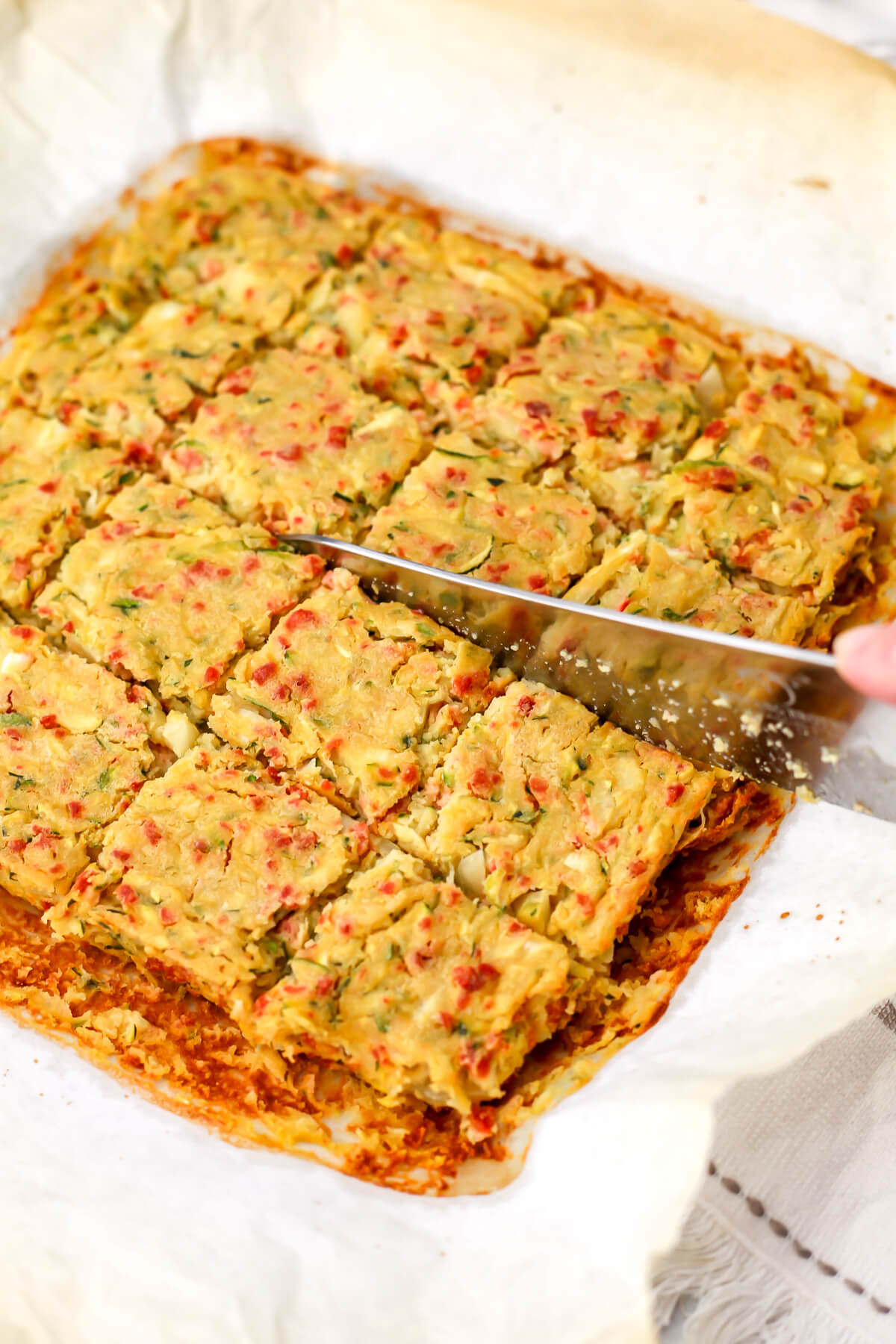 Vegan zucchini slice being cut into squares with a large knife.
