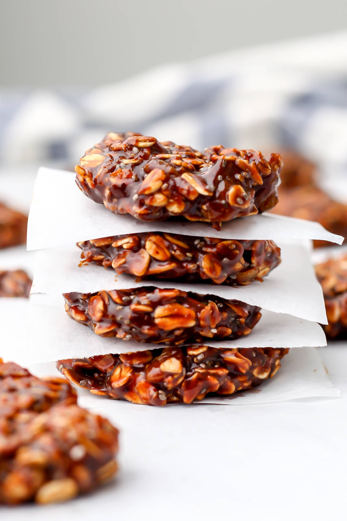 Healthy almond butter no-bake cookies stacked on parchment paper with a blue and white tea towel behind them.
