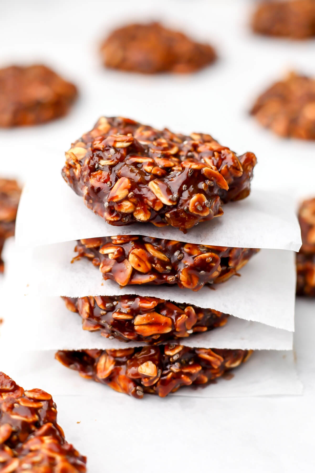A stack of vegan almond butter no-bake cookies on white parchment paper.