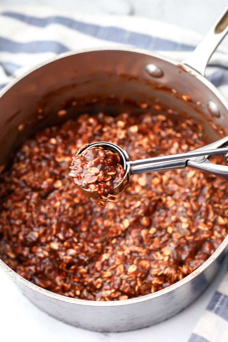 A cookie scoop with almond butter no-bake cookie mixture in in over a saucepan.