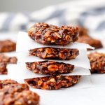 Almond butter no bake cookies stacked on parchment paper with a blue and white tea towel behind it.