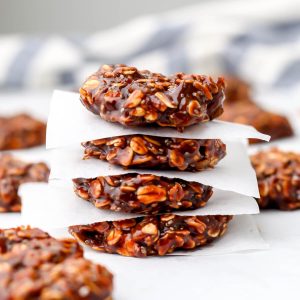 Almond butter no bake cookies stacked on parchment paper with a blue and white tea towel behind it.
