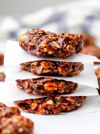 Almond butter no bake cookies stacked on parchment paper with a blue and white tea towel behind it.