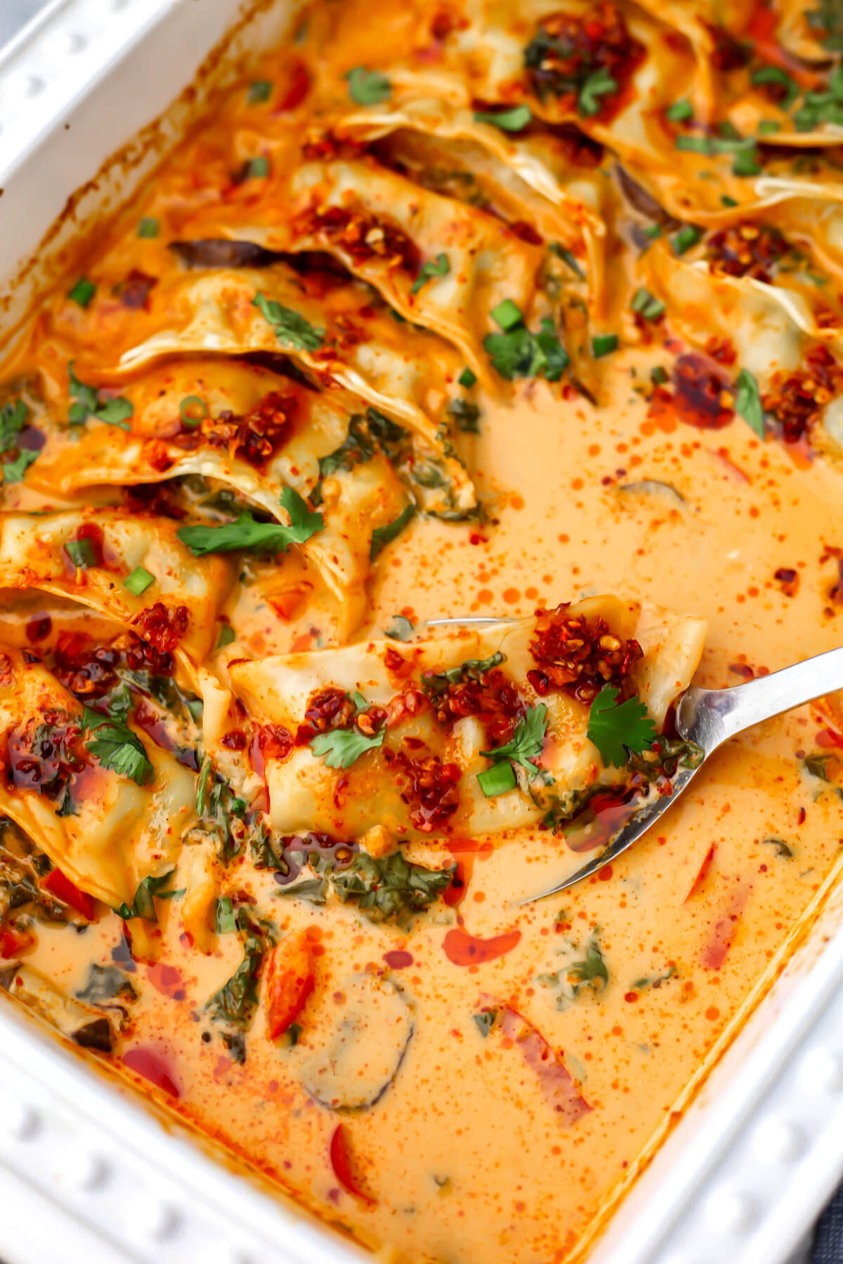 A white baking dish filled with vegan dumplings baked in a red curry coconut sauce.