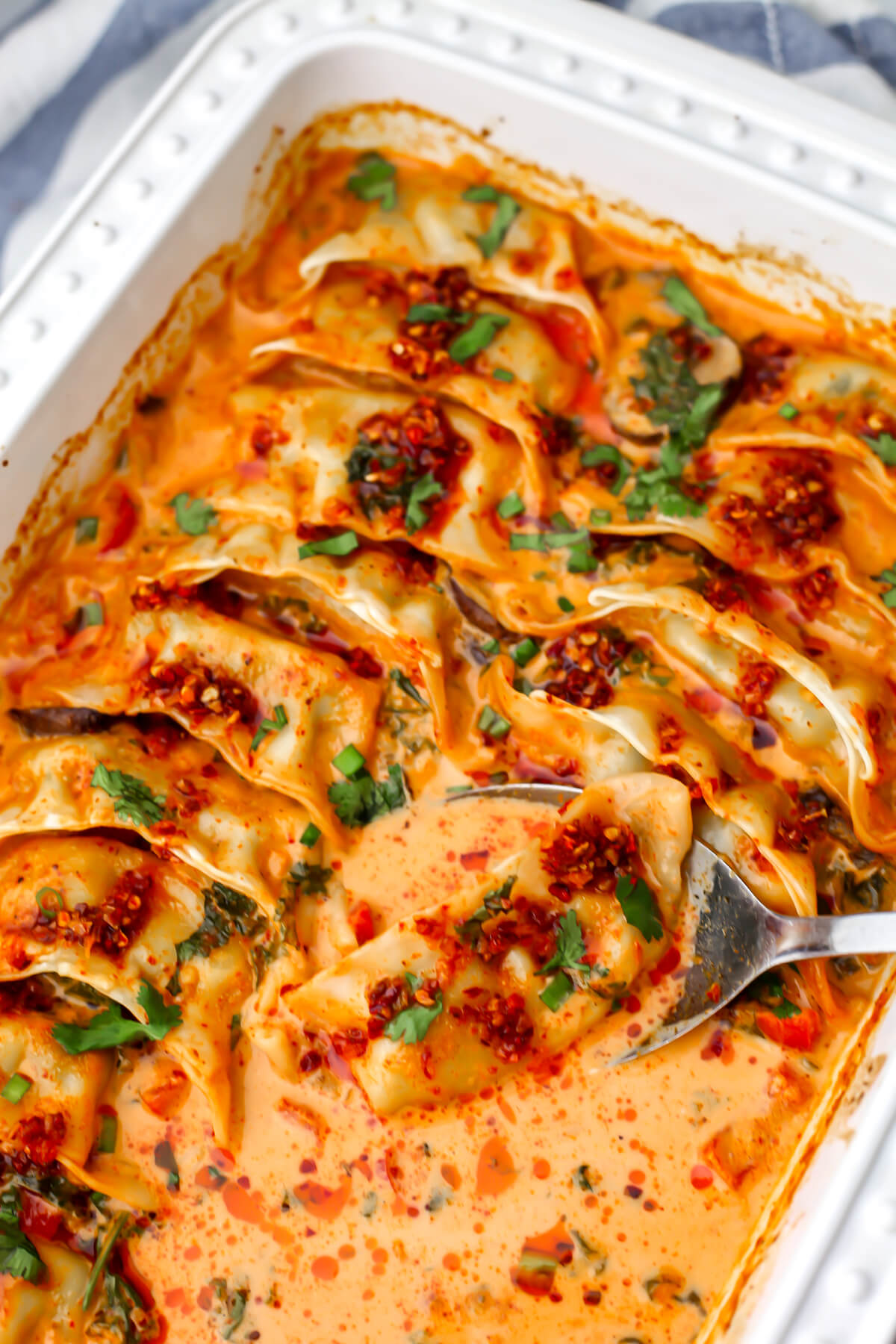 A baking dish filled with vegan baked dumplings with a spoon scooping one out of the dish.