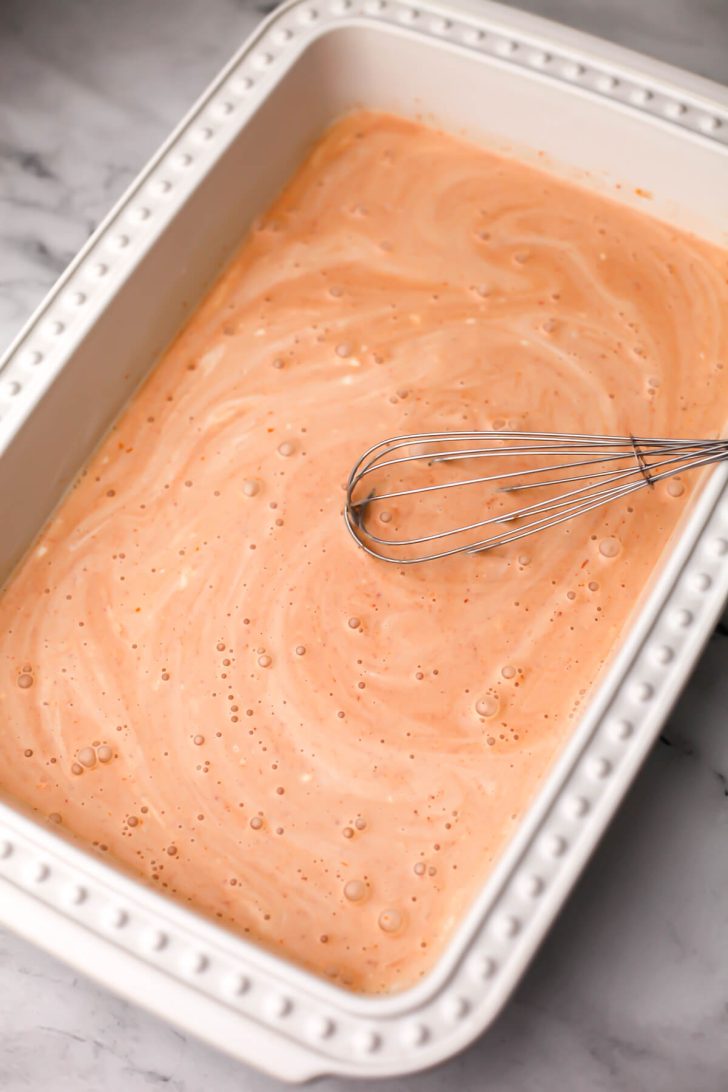 Vegan red curry coconut sauce being stirred in the bottom of a baking dish.