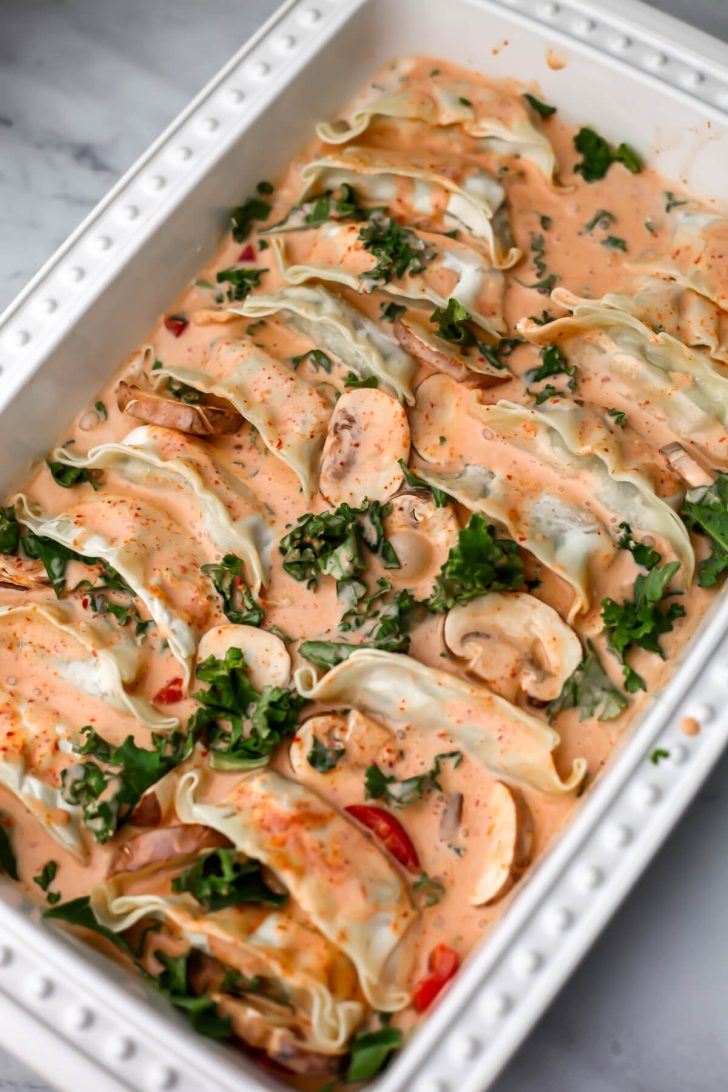 Frozen vegetable dumplings added to red curry sauce and vegetables in a baking dish.