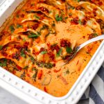 A white baking dish with a spoon scooping out a vegan dumpling baked in a red curry coconut milk sauce.