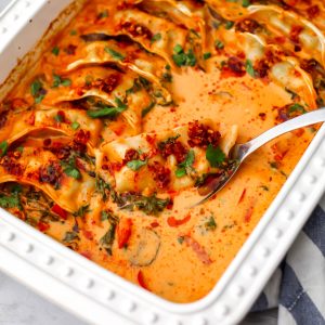 A white baking dish with a spoon scooping out a vegan dumpling baked in a red curry coconut milk sauce.