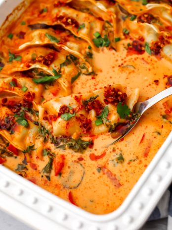 A white baking dish with a spoon scooping out a vegan dumpling baked in a red curry coconut milk sauce.