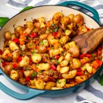 Vegan breakfast sausage made with onions, peppers, potatoes, and vegan sausage in a blue skillet being stirred with a wooden spoon.