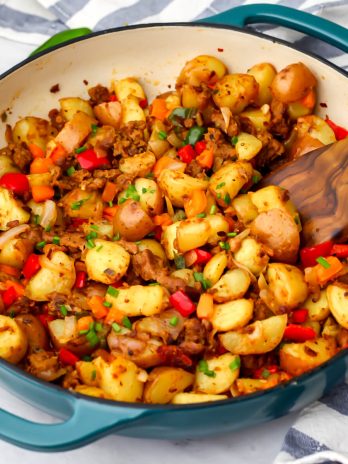 Vegan breakfast sausage made with onions, peppers, potatoes, and vegan sausage in a blue skillet being stirred with a wooden spoon.