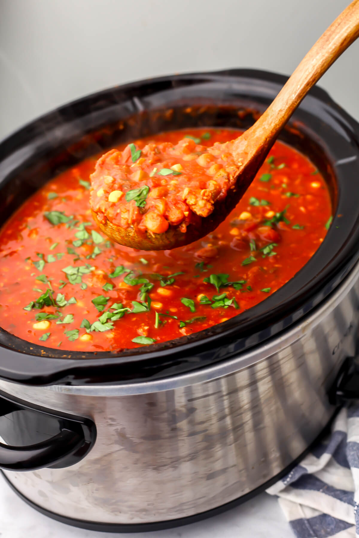 A crockpot filled with vegan chili being scooped up with a wooden ladle.