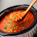 A large slow cooker filled with vegan chili being scooped up with a wooden ladle.