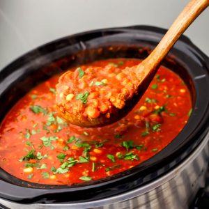 A large slow cooker filled with vegan chili being scooped up with a wooden ladle.