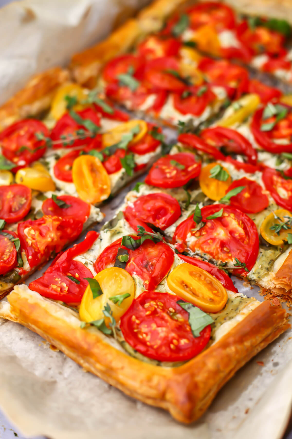 A close up of a vegan tomato tart with yellow and red tomatoes topped with thyme and chopped basil.