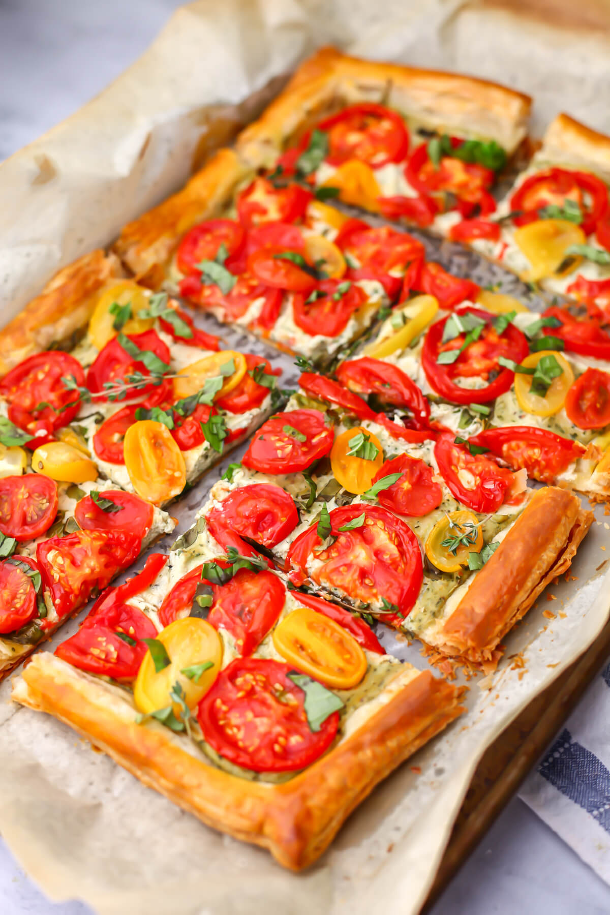 A vegan tomato tart made with puff pastry on a parchment lined baking sheet.