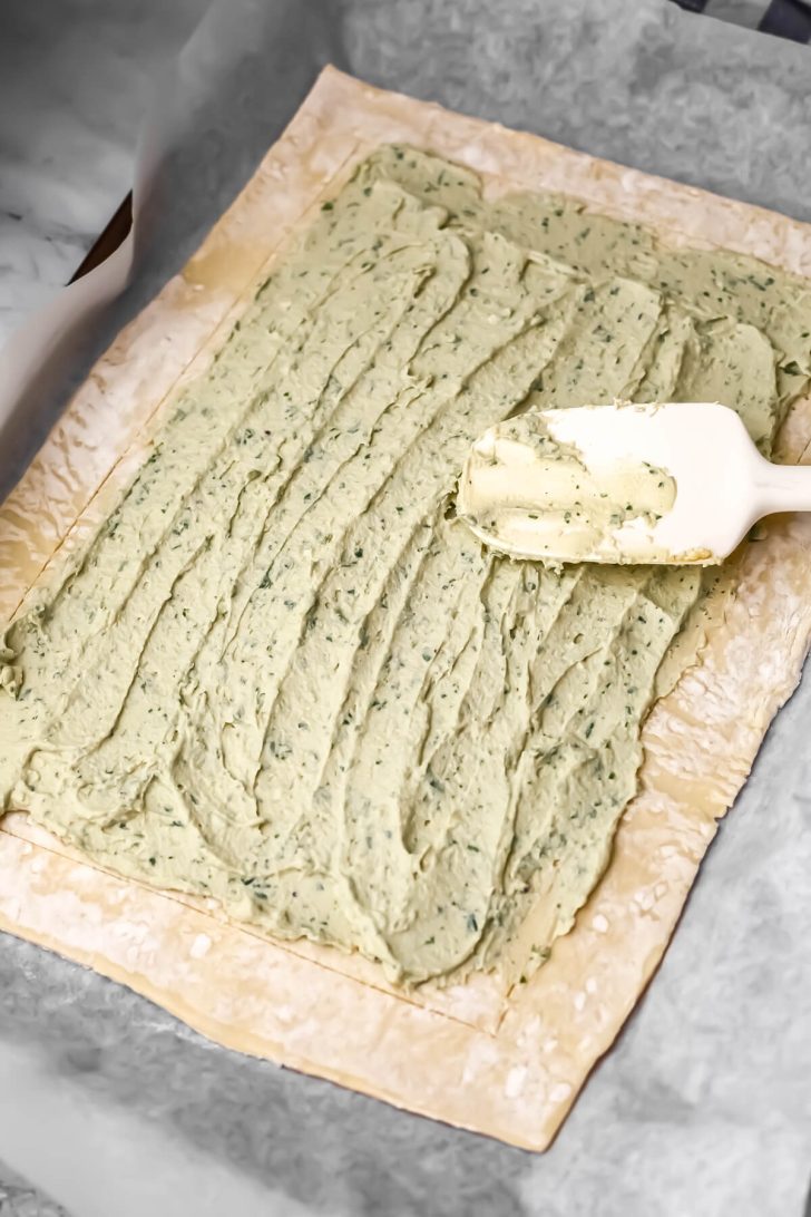 A puff pastry with tofu ricotta being spread in the cent of it to make a tomato tart.
