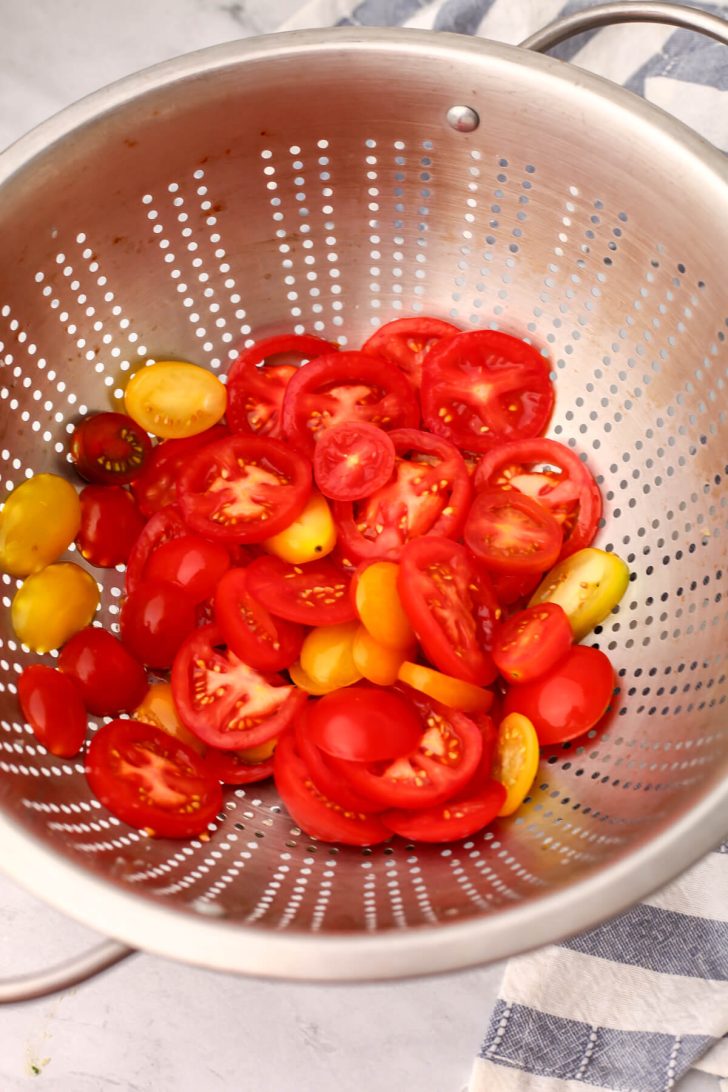 Sliced tomatoes in a colander sprinkled with salt.